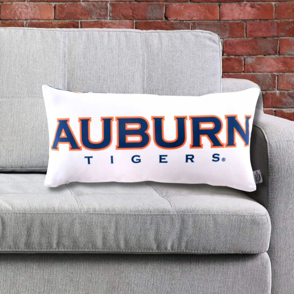 Auburn Tigers logo pillow on a gray couch against a brick wall.