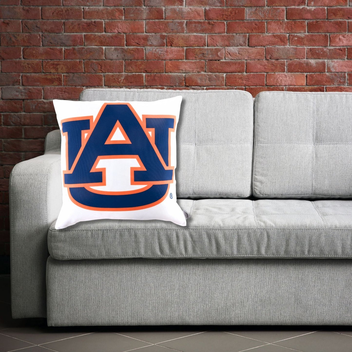 Gray sofa with an Auburn University logo pillow against a brick wall.