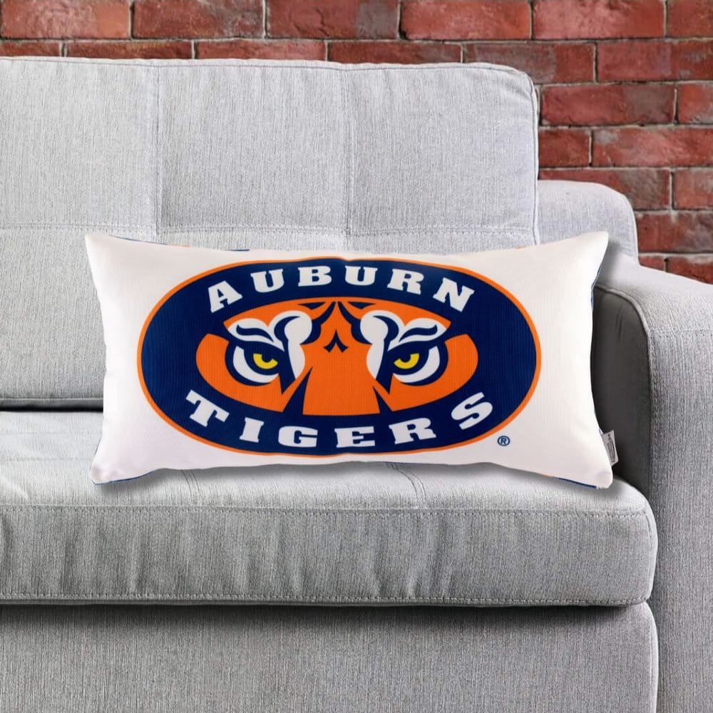 Auburn Tigers Eyes logo pillow on a gray couch against a brick wall.