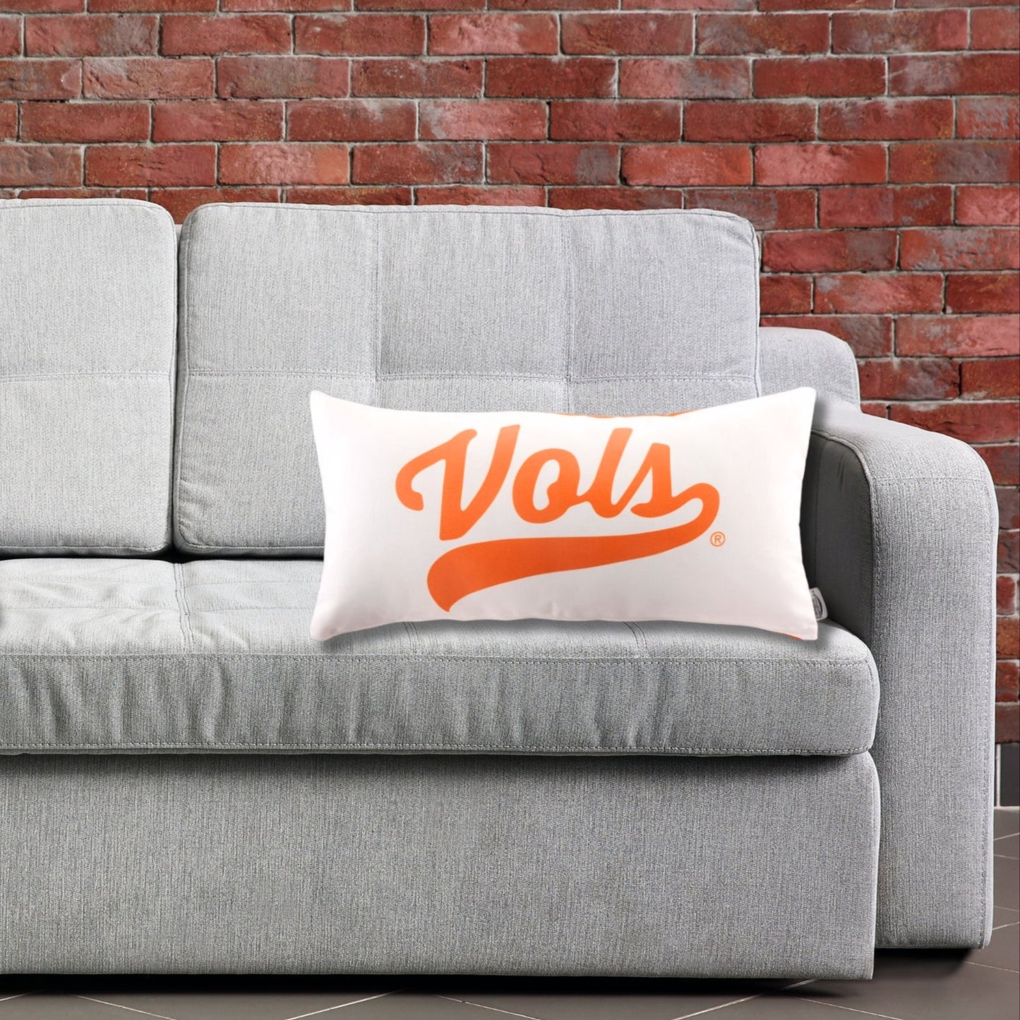 Gray sofa with 'TENNESSEE VOLS' lumbar throw pillow against a brick wall. In a mancave setting.