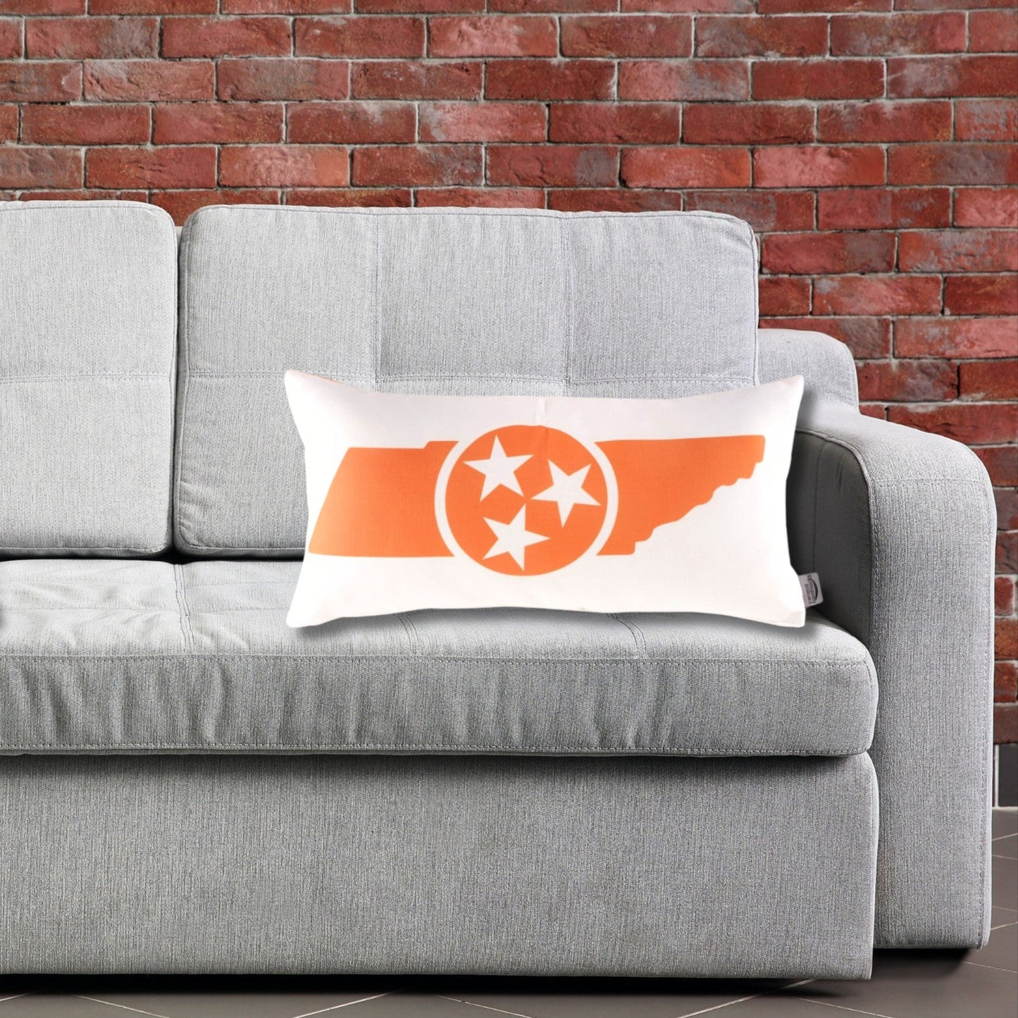 Gray sofa with Tennessee Volunteers-themed pillows against a brick wall.