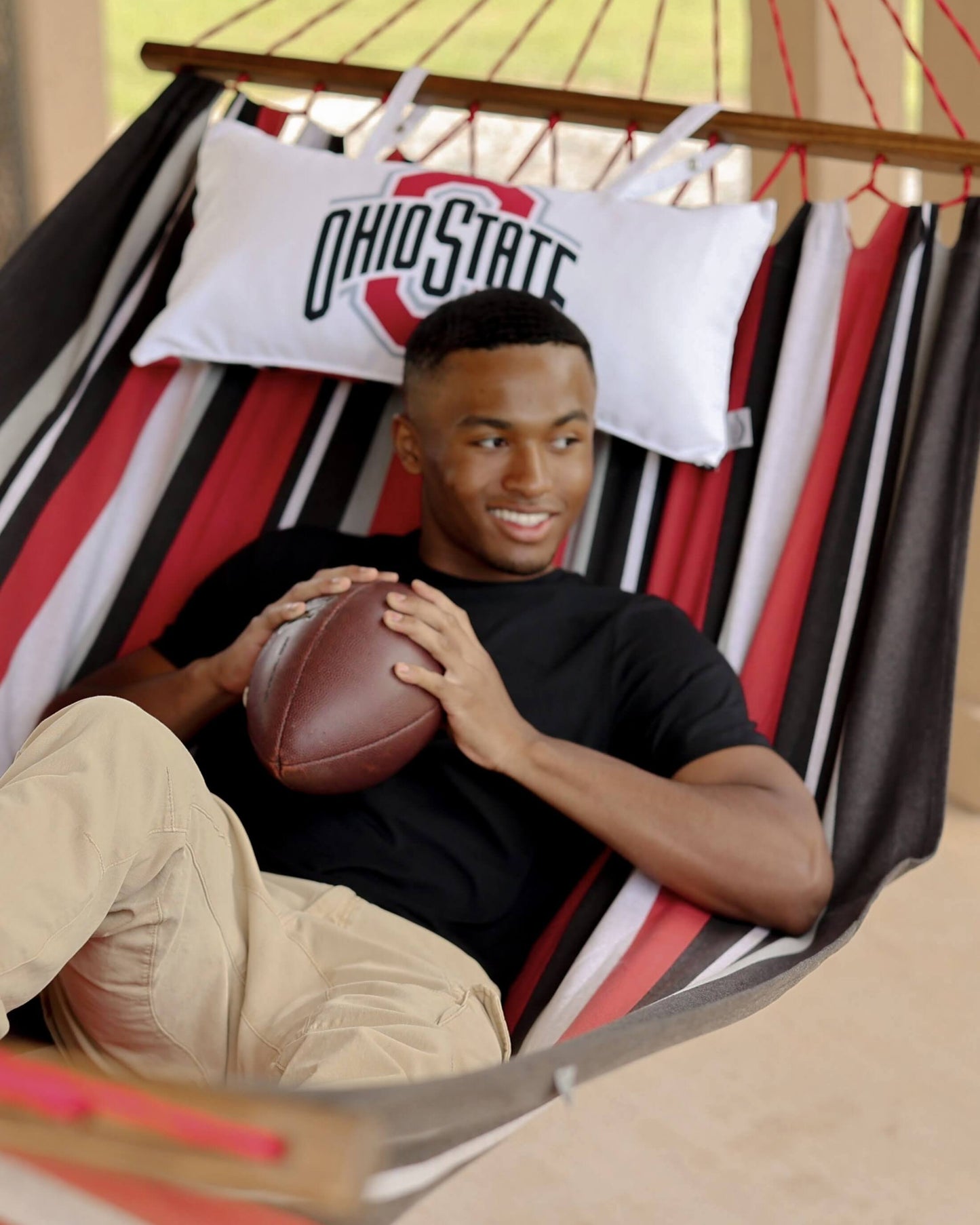 Man holding a football in a hammock with an Ohio State pillow