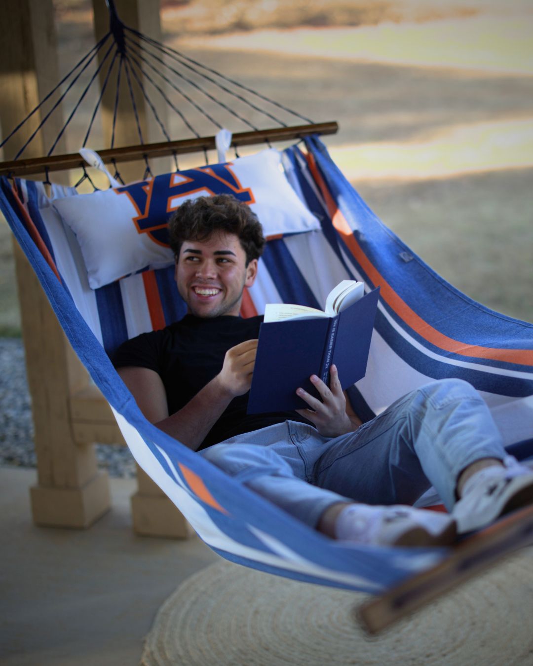 Man reading a book in a blue, orange and white hammock with the Auburn Tigers logo outdoors