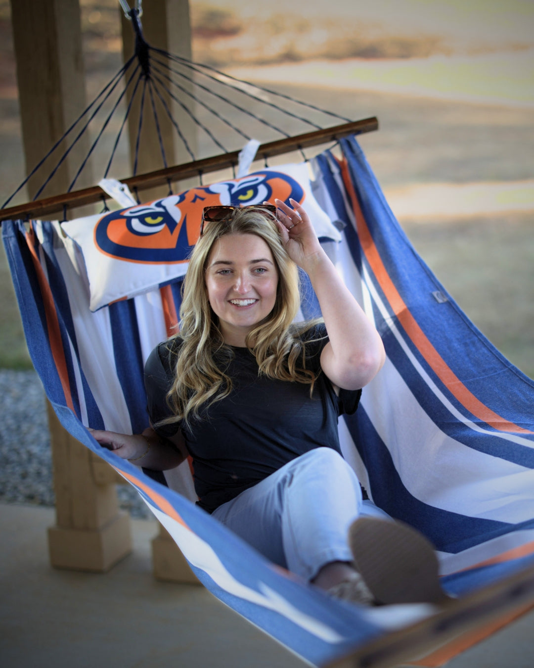Woman sitting in a striped blue and orange Auburn University hammock with colorful pillows.