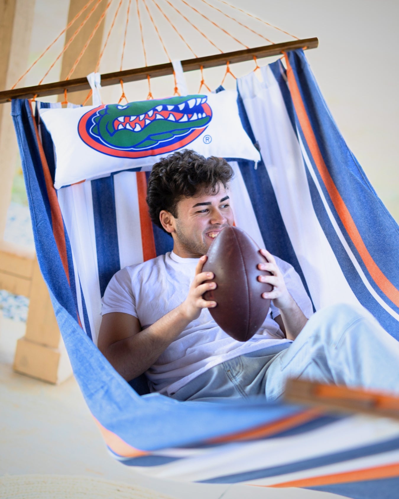 Person holding a football in a hammock with a pillow featuring a Florida Gator athletic logo outside tailgating.