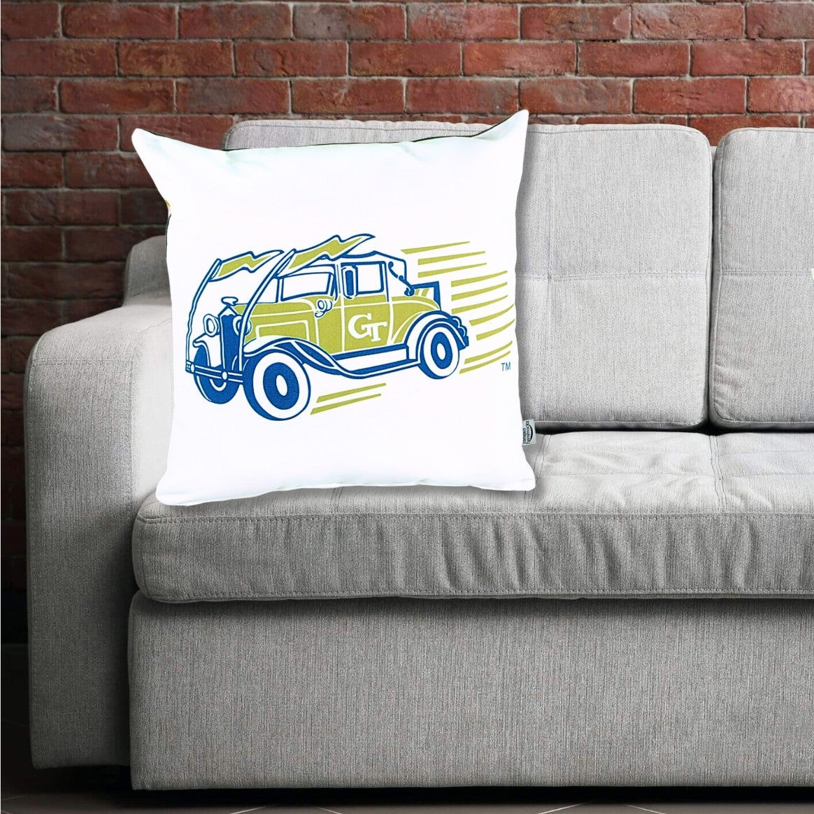 Two pillows on a gray sofa with one featuring a vintage car design Ramblin Wreck and the other displaying 'Georgia Tech' text.
