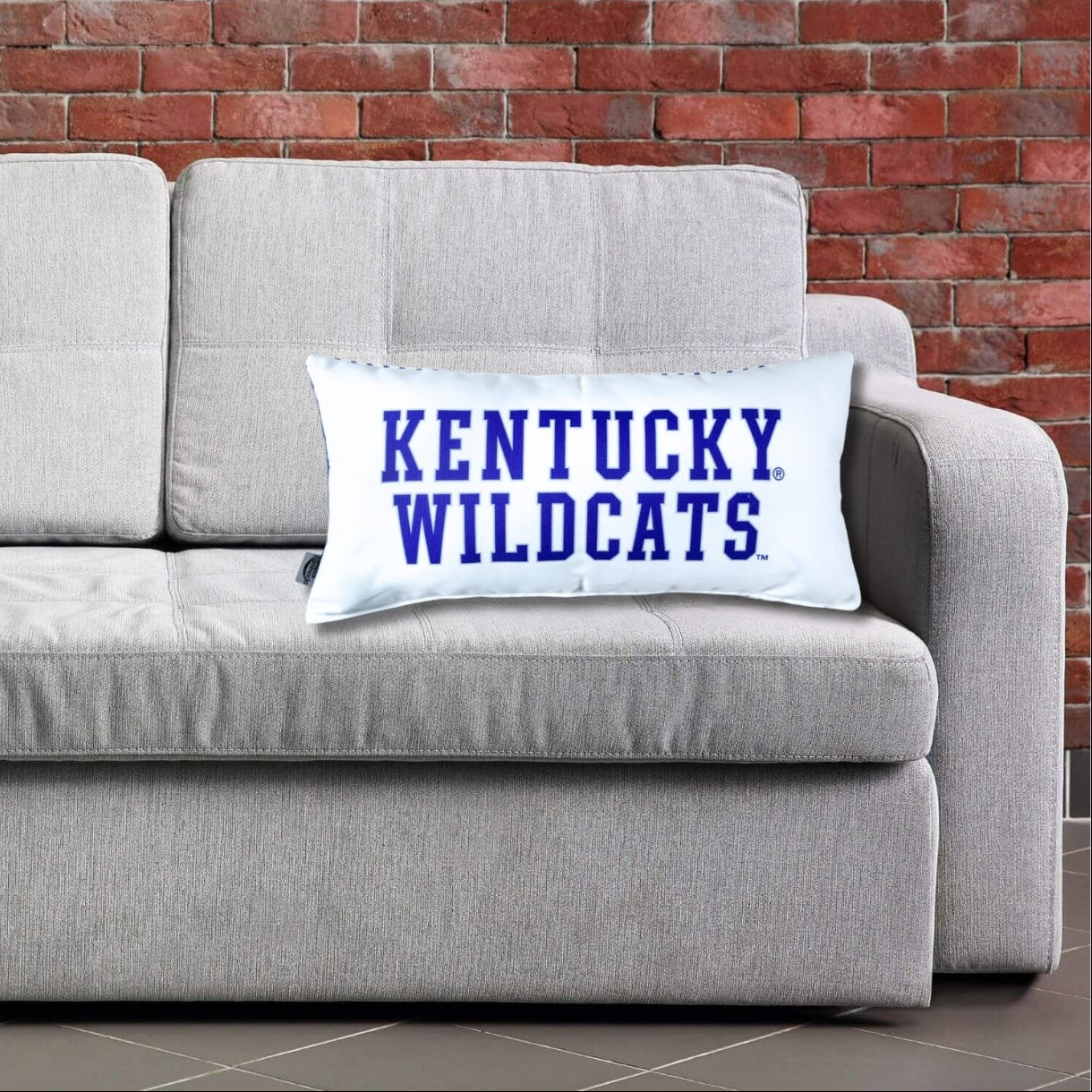 Gray sofa with 'Kentucky Wildcats' pillows against a brick wall.