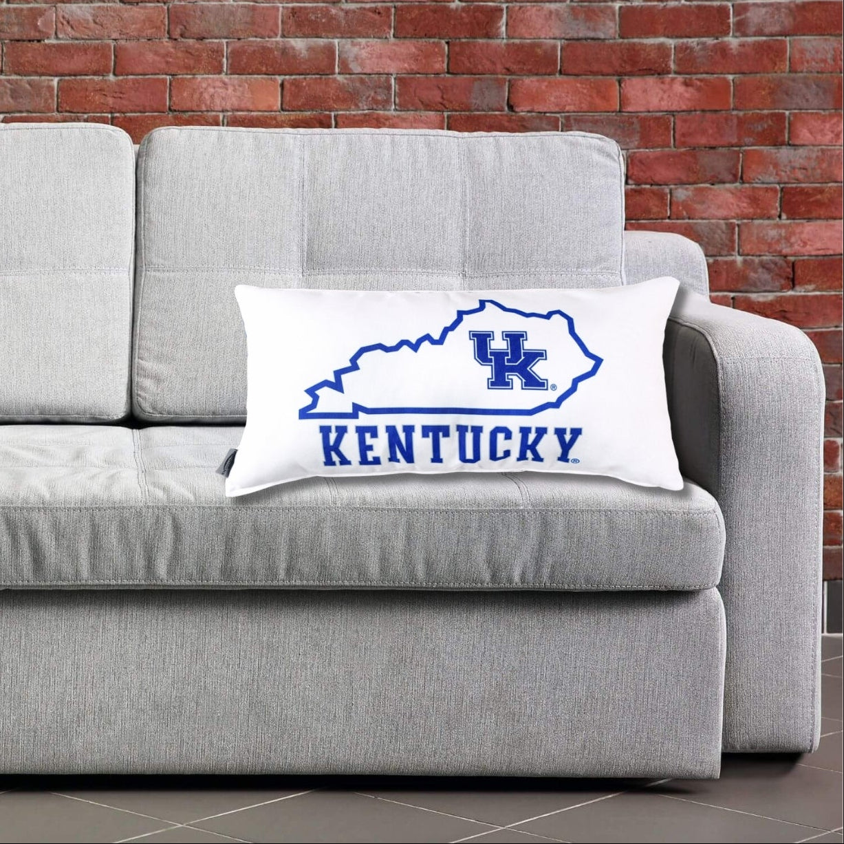 A Kentucky logo pillow on a gray couch against a brick wall. Home Decor for University of Kentucky Dorm