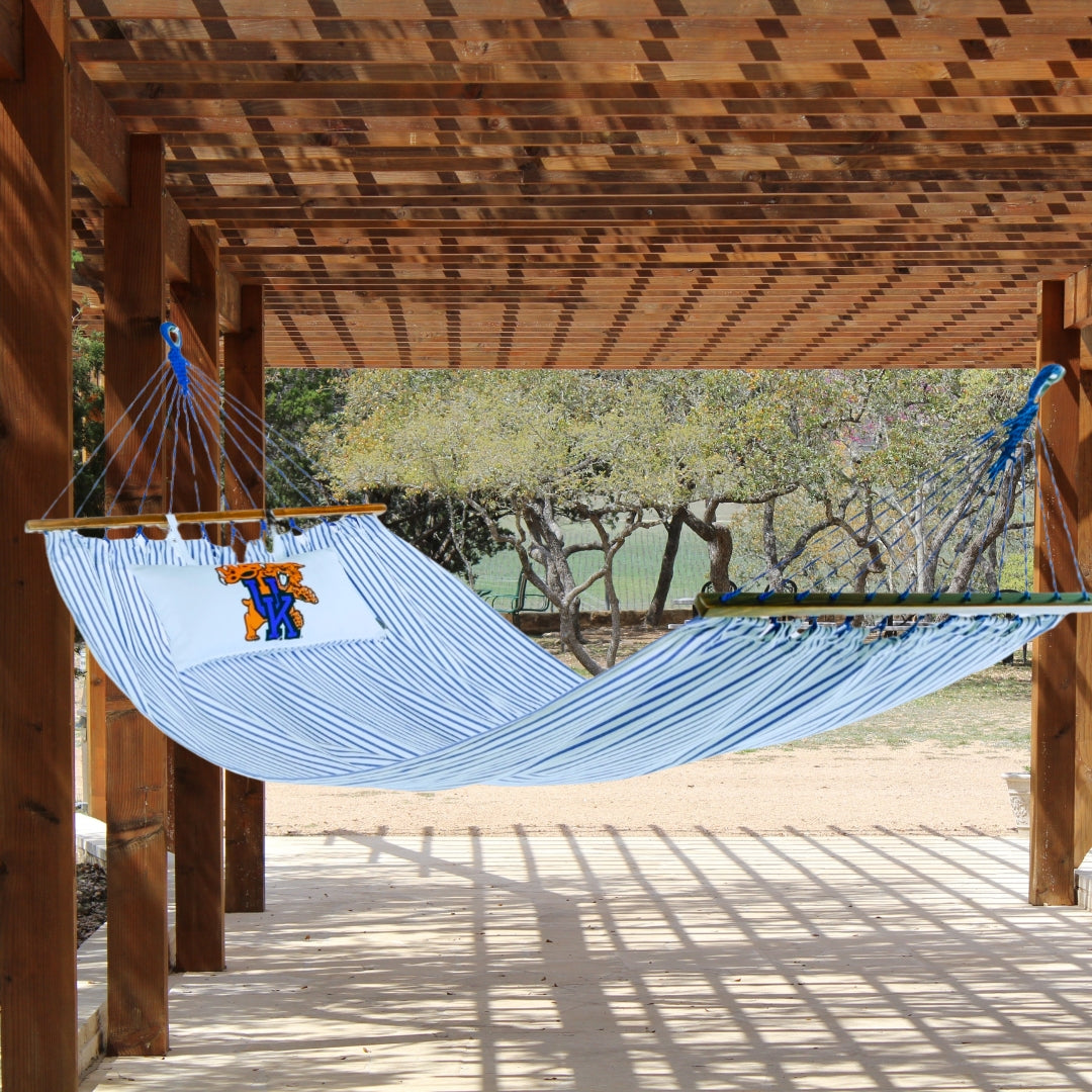 Blue UK wildcats hammock with a pillow on a wooden deck with a view of trees in the background