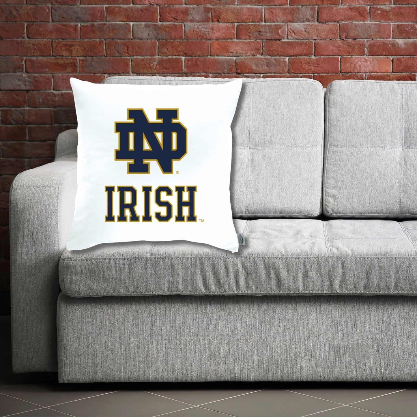Gray sofa with a pillow featuring ND Irish logo against a brick wall.