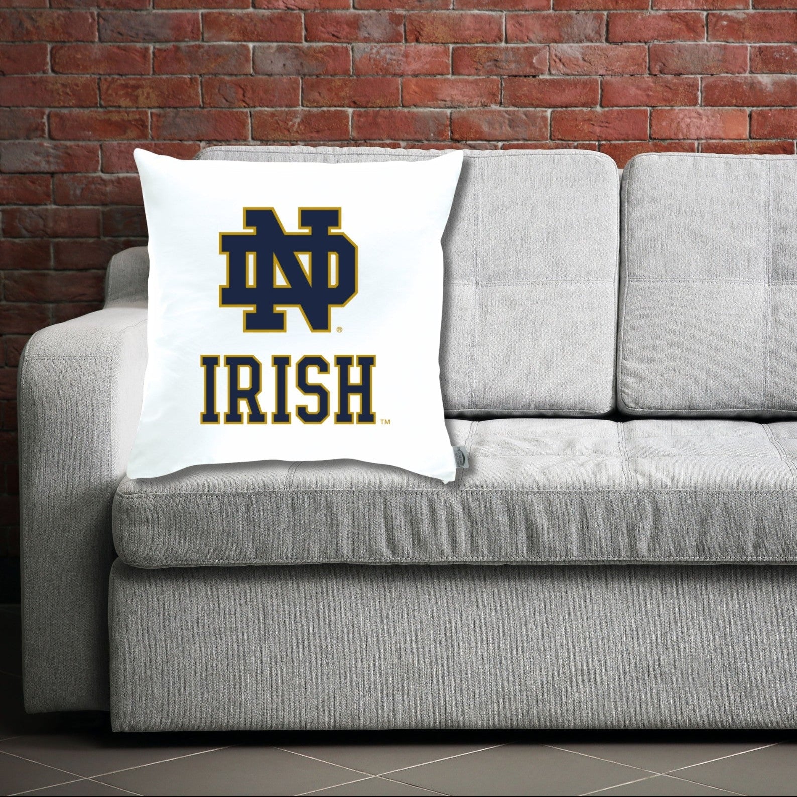 Gray sofa with a pillow featuring ND Irish logo against a brick wall.