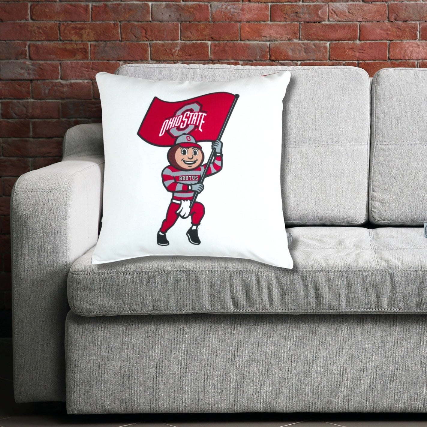 Pillows with Ohio State-themed design  featuring Brutus Buckeye on a gray couch against a brick wall.