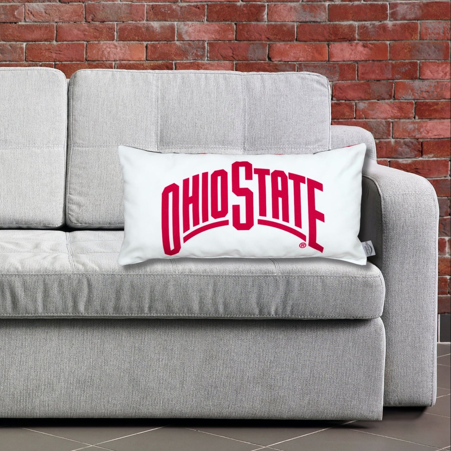 Gray sofa with pillows featuring Ohio State-themed designs against a brick wall.