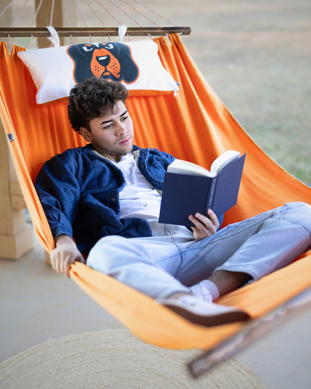 Person reading a book in an orange UTK Tennessee hammock with a Smokey dog-themed pillow.