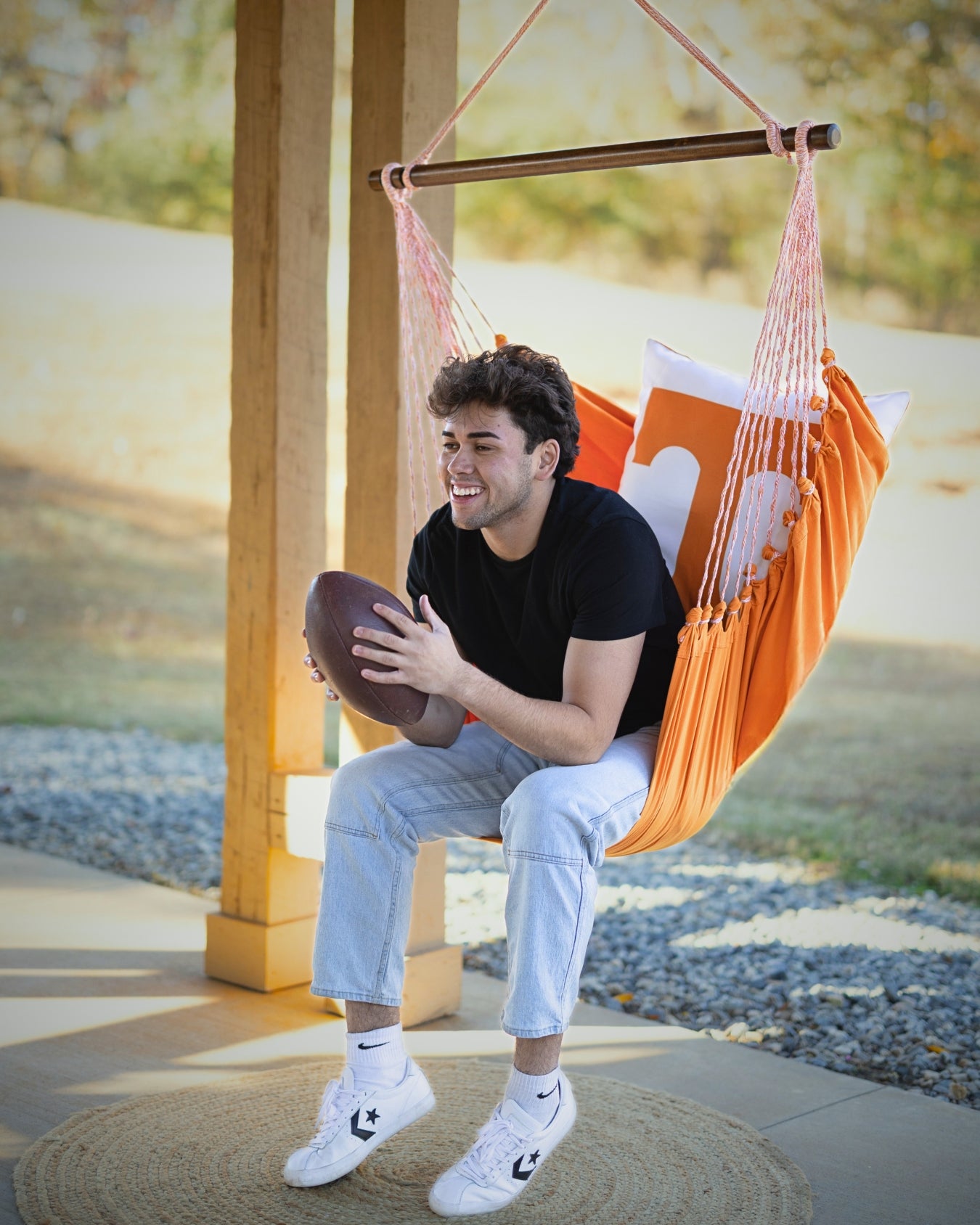 man sitting in an orange Vols Power T logo hammock holding a football outdoors