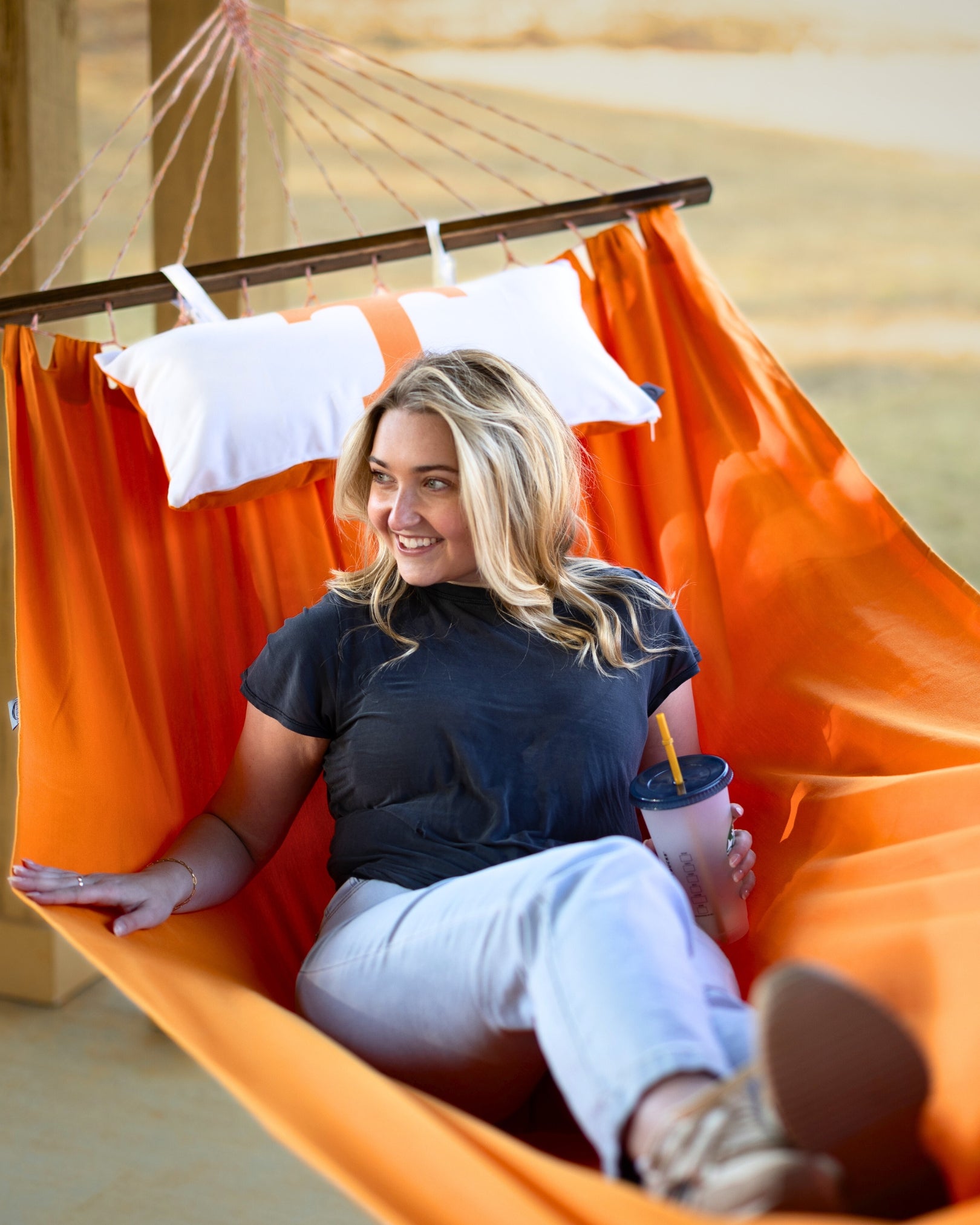 Woman sitting in a Tennessee orange hammock holding a drink, with a blurred outdoor background