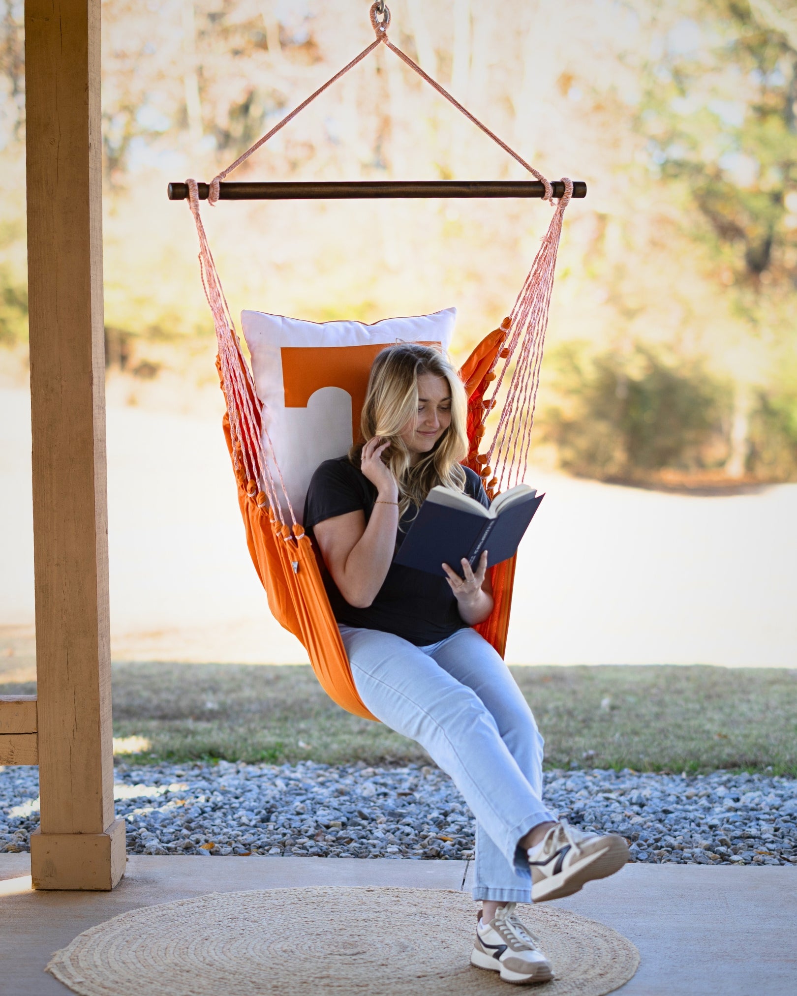 Woman reading a book in an orange UTK Tennessee hammock chair outdoors.