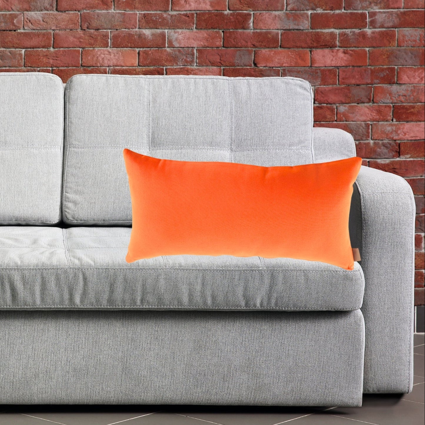 Gray sofa with  Tennessee orange pillow cushions against a brick wall