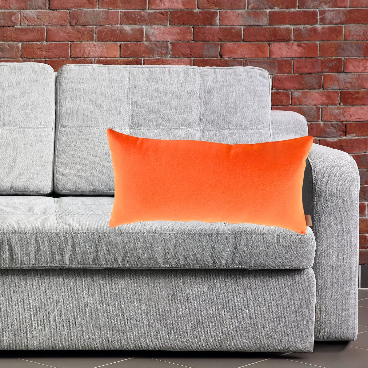 Gray sofa with  Tennessee orange pillow cushions against a brick wall