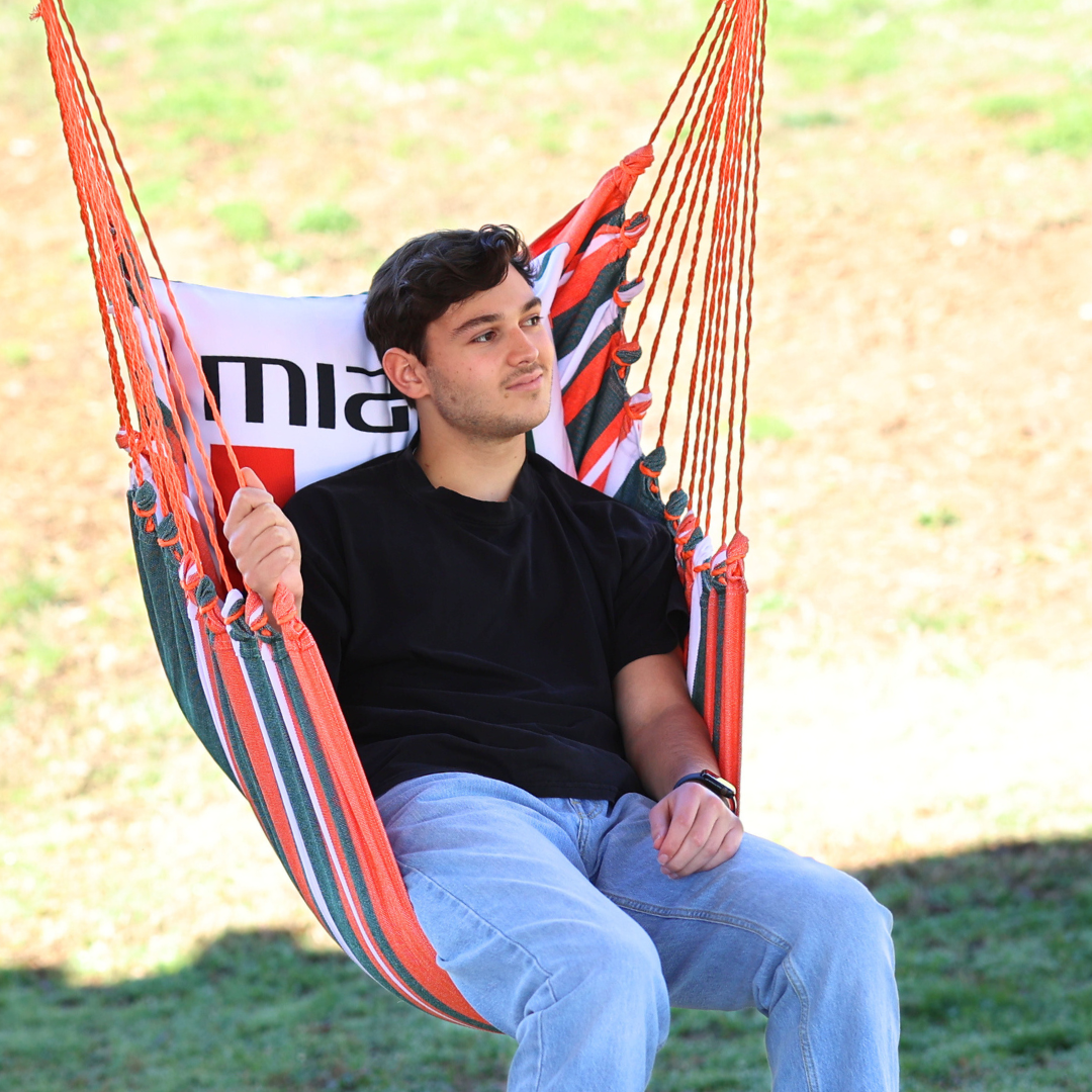 Man sitting in a striped Miami Hurricanes hammock with a blurred background