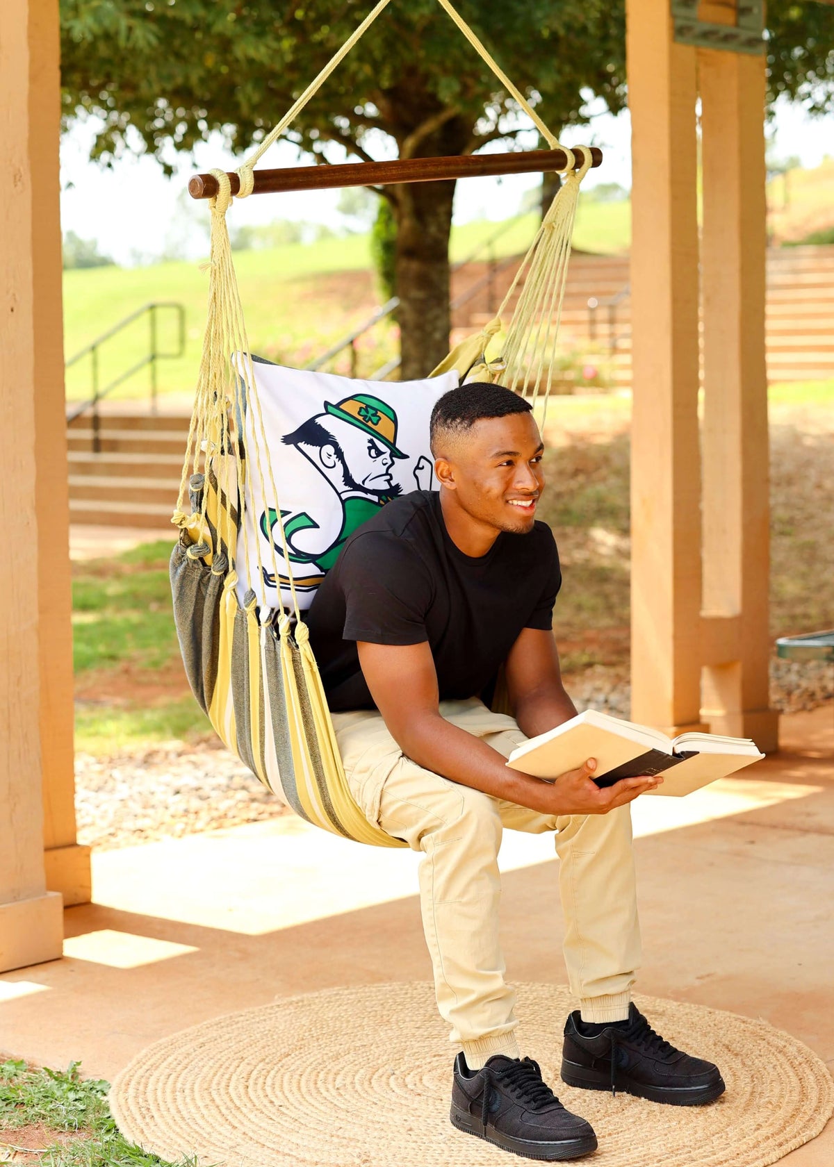 Man reading in a Notre Dame Leprechaun hammock chair on a covered patio