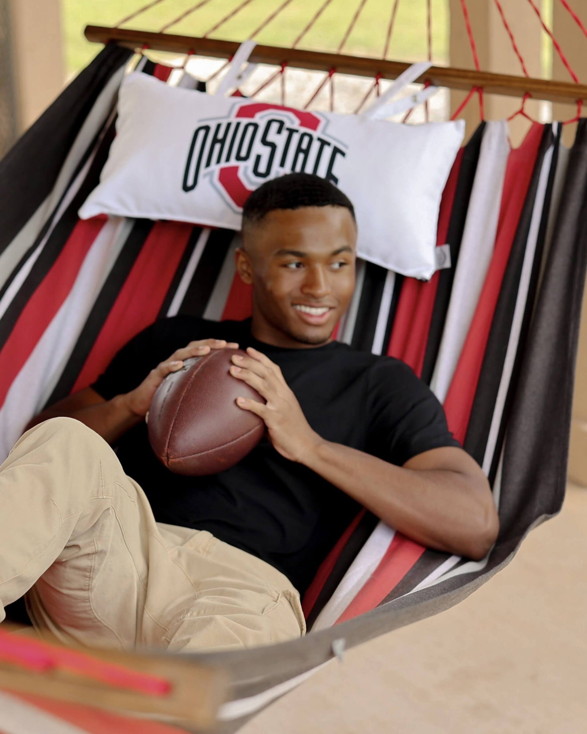 Man holding a football in a hammock with an Ohio State pillow